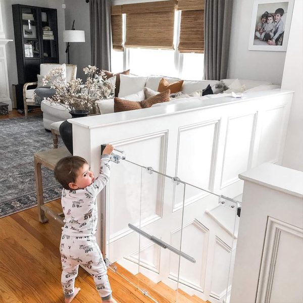 A toddler is at the top of a staircase attempting to open the Fred Screw Fit Clear View Safety Gate.
